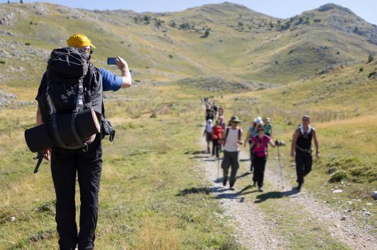 Guide de randonnée qui prend une photo de son groupe de randonneur sur un sentier au milieu des collines