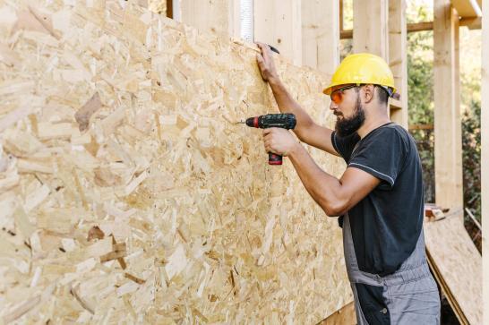 Ouvrier qui fixe une paroi en bois sur une structure de maison en bois