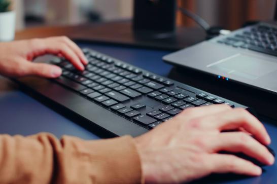 Homme qui utilise un ordinateur, il a une main sur la souris et l'autre sur le clavier
