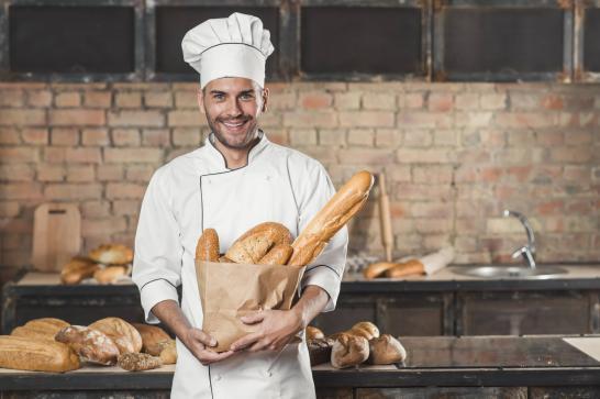 Boulanger dans son atelier qui tient dans un sac du pain et une baguette