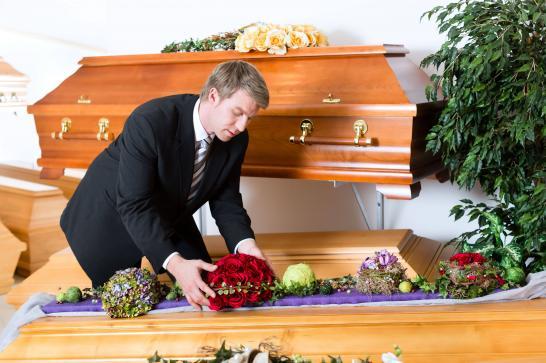 Agent de pompes funèbres qui dépose une gerbe de fleurs sur un cercueil