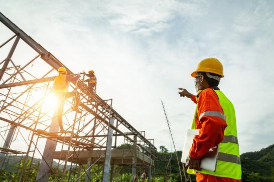Gestionnaire de chantier de construction en tenue de sécurité qui donne des indications à des hommes en train de travailler sur une charpente métallique.