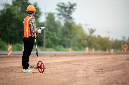 Métreur deviseur sur un chantier de route. Il tient dans ses mains une tablette et un odomètre