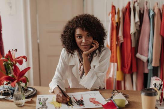 Femme styliste qui pose alors qu'elle est en train de dessiner des robes dans son atelier de couture