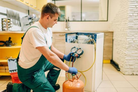 Technicien qui remplit de gaz un réservoir de frigo
