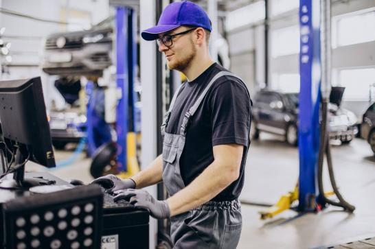 Technicien automobile qui consulte son ordinateur dans le garage afin de trouver l'origine d'une panne