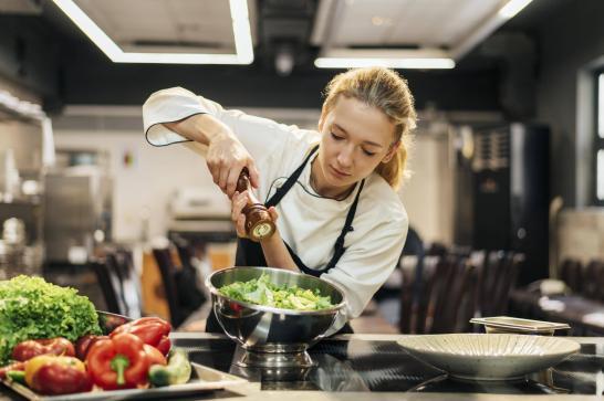 Cuisinière dans sa cuisine de restaurant en train d'assaisonner une salade