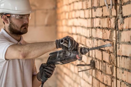 Ouvrier qui fait une saignée dans un mur de brique dans une maison en rénovaton
