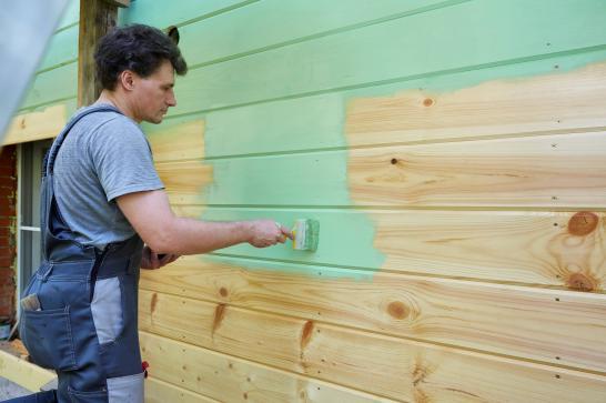 Peintre en bâtiment qui peint une paroi extérieure en bois