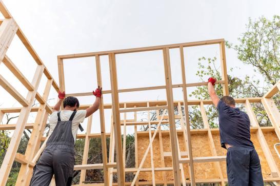 Techniciens en construction bois en train de soulever une structure de mur d'une maison en bois