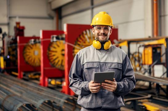 Opérateur technique industriel avec une tablette et ses équipements de sécurité près d'une ligne d'assemblage industrielle