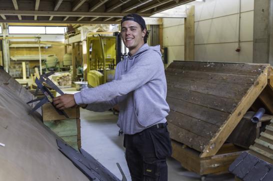 Photo d'un apprenant qui manipule des outils de couvreur et regarde la caméra avec le sourire.