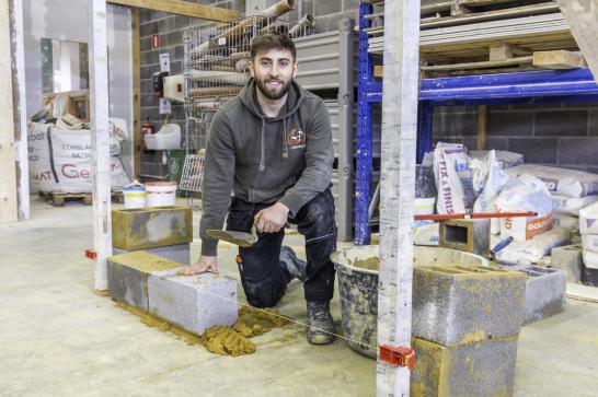 Photo d'un apprenant qui maçonne et regarde la caméra avec le sourire.