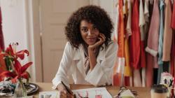 Femme styliste qui pose alors qu'elle est en train de dessiner des robes dans son atelier de couture